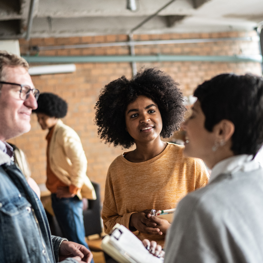 Professionals having a conversation during a networking event, woman in orange sweater listening attentively.